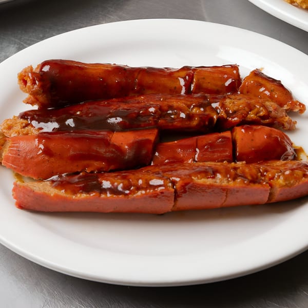 A white plate holds several pieces of sliced BBQ sausage covered in a rich, dark sauce.