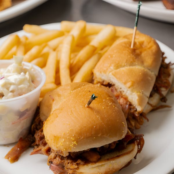 Two pulled pork sliders with a side of golden french fries and coleslaw on a white plate.