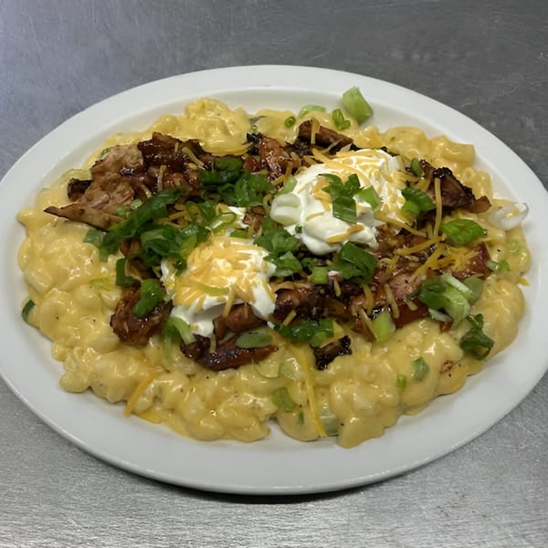 Creamy mac and cheese topped with BBQ meat, shredded cheese, sour cream, and green onions.