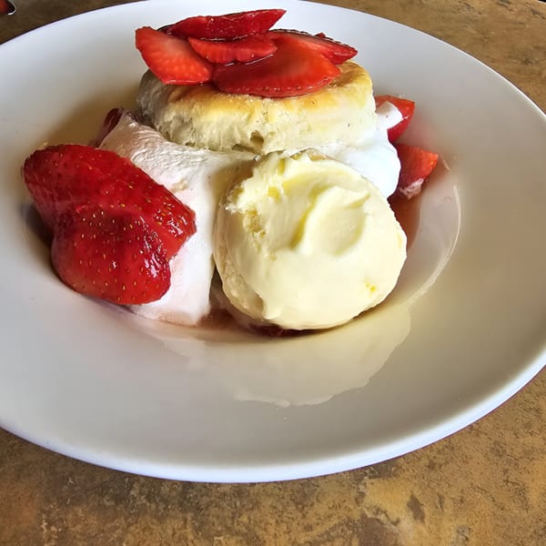 Strawberry shortcake with whipped cream and a scoop of vanilla ice cream on a white plate.
