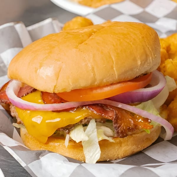 A bacon cheeseburger with lettuce, tomato, and red onion, served in a checkered paper tray.