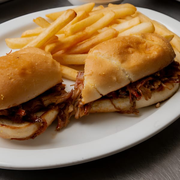 Two BBQ pulled pork sandwiches with golden french fries on a white plate.